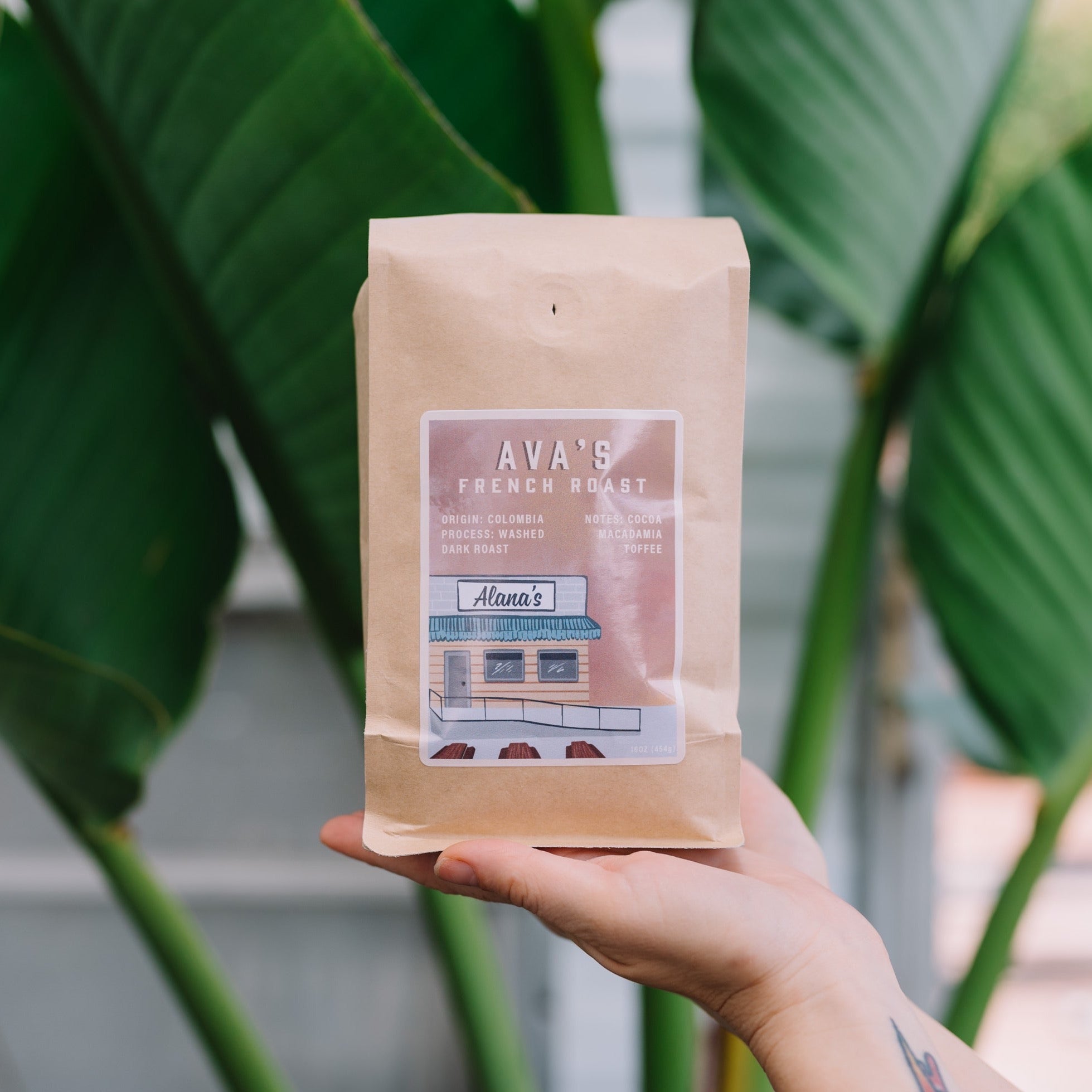 A bag of Alana's Coffee Roasters' Ava's French Roast coffee beans. The label depicts a sketch of Alana's Mar Vista location on a mauve backdrop.