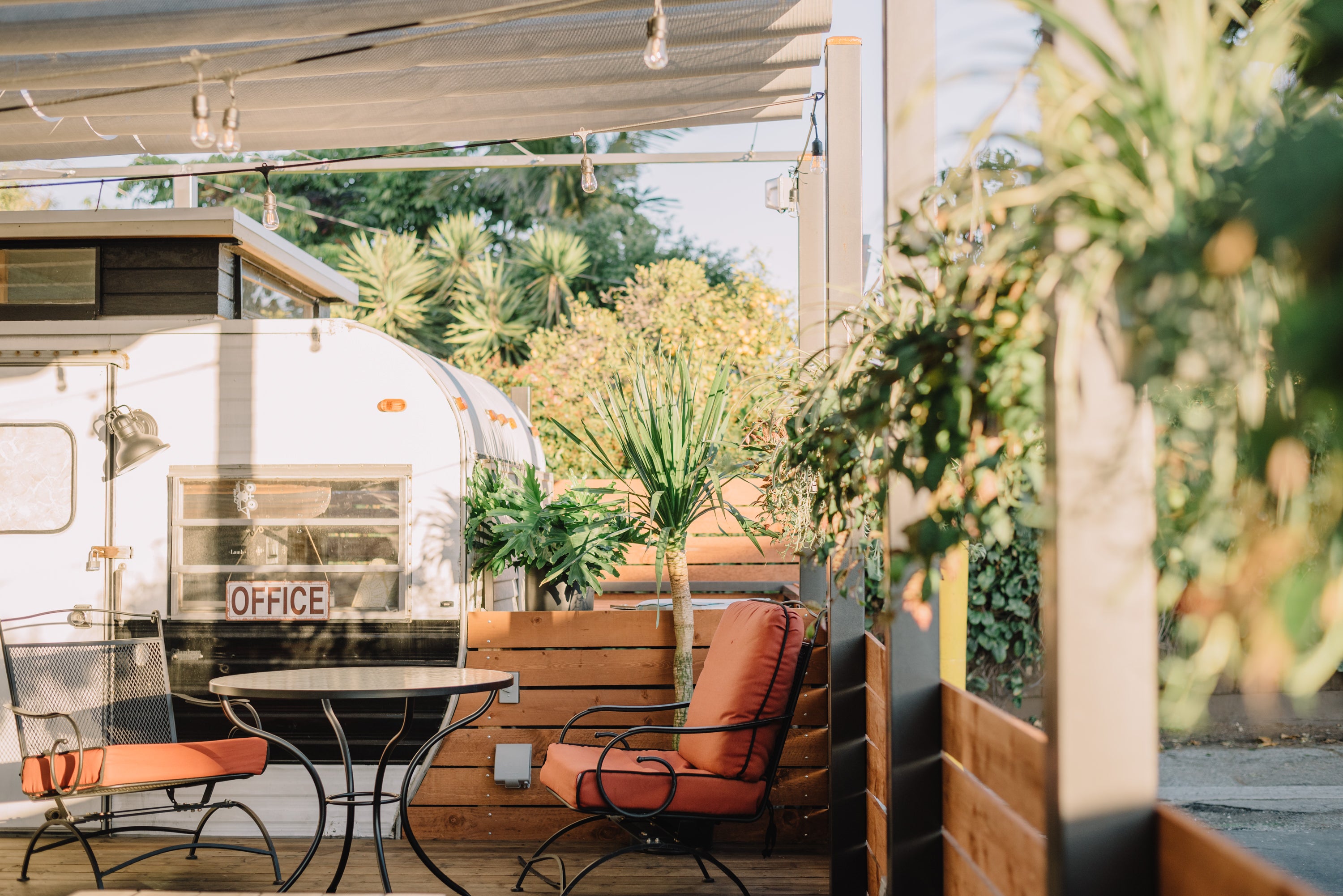 The white office trailer behind the patio at Alana's in Mar Vista. Potted plants and patio furnishing sit around the entrance to the trailer.