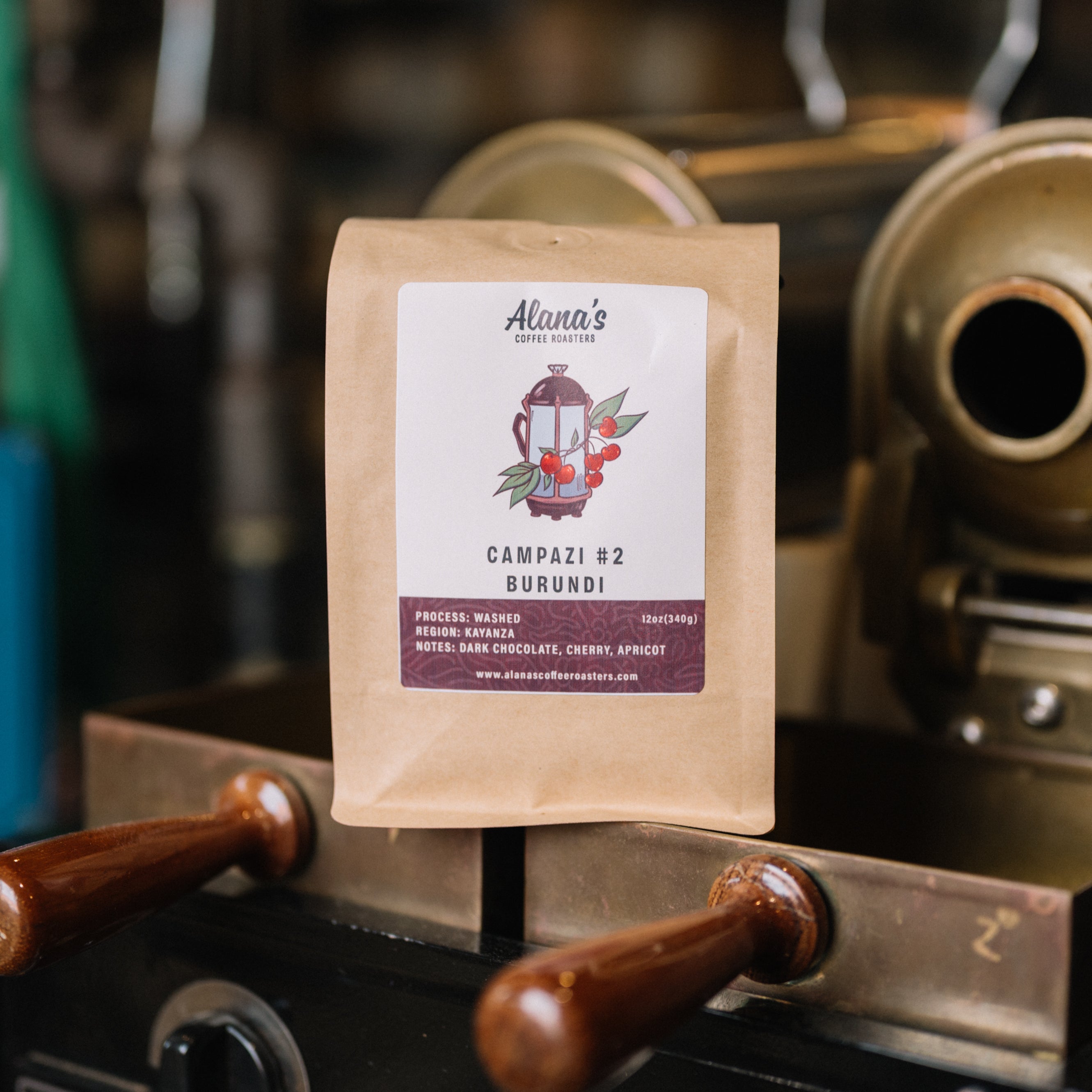 Alana's Coffee Roasters Campazi #2 Burundi bag on a coffee roasting machine with roasted beans nearby.