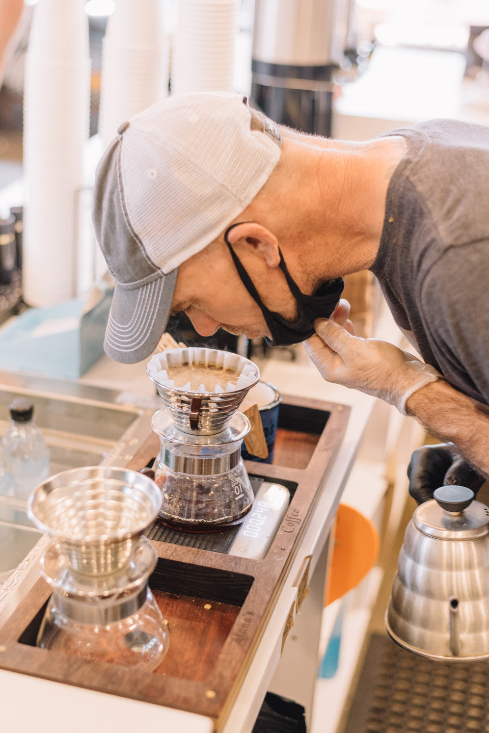 A man bends down and takes off his mask to smell the coffee being brewed. 